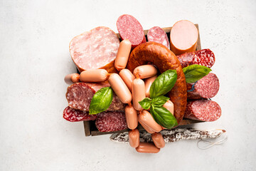 Set of different types of sausages, salami and smoked meat with basil in a box on white background. Top view.