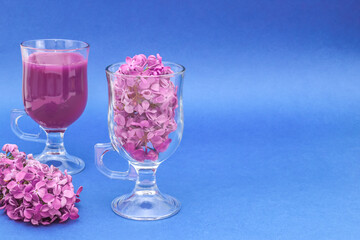 Lilac flowers and a drink in glasses.
Lilac flowers and a drink in glasses stand on the left against a blue background with space for text on the right, close-up side view.