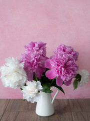 Bouquet of white and pink peonies in a white jug on a pink background. Close-up, selective focus