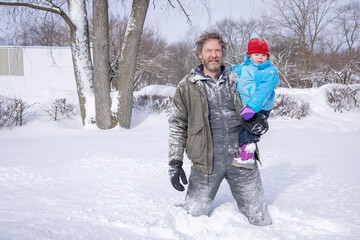 Fototapeta na wymiar Dad and daughter playing in the snow in their backyard on a cold snowy day