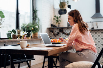 Young woman working at home in the kitchen with a laptop.