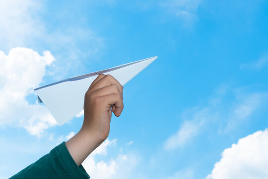 Toy paper airplane in child hand against cheerful blue sky with white clouds. Children dreams, inspirations and the future concept.
