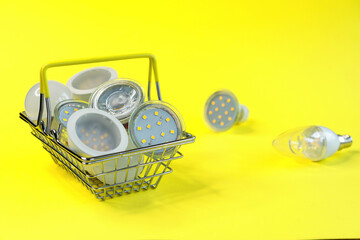 LED energy saving lamps in a metal shopping basket on a yellow background.