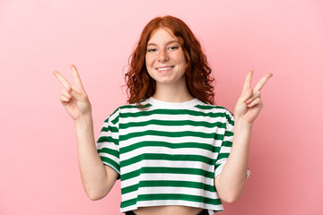 Teenager redhead girl over isolated pink background showing victory sign with both hands