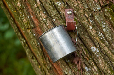 A metal mug for water with a chain near a source