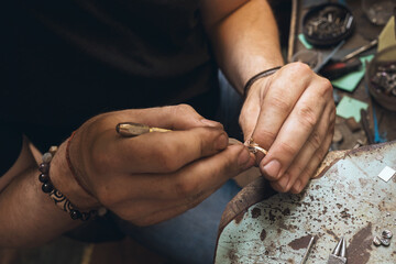 A jeweler is taking apart a gold ring with stones in a workshop, close-up