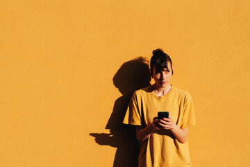 Modern woman browsing smartphone near yellow background