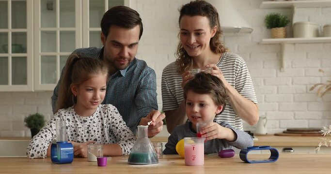 Interested joyful small children siblings involved in doing chemical experiments with loving caring couple parents in modern kitchen, enjoying learning with game, educating with entertainment.