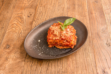Beef lasagna with a lot of meat and a lot of tomato with grated cheese and several sheets of pasta between the meat, all topped with some basil leaves