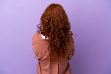 Teenager redhead girl over isolated purple background in back position