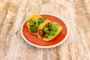 Two pastor tacos with corn tortillas with coriander and basil on red plate and wooden table