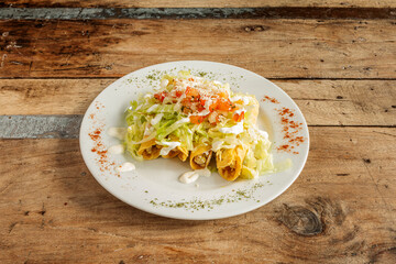Plate of Mexican golden tacos with lettuce and salsa on top