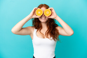 Teenager redhead girl isolated on blue background in swimsuit and holding an orange