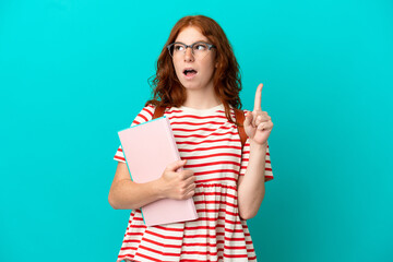 Student teenager redhead girl isolated on blue background thinking an idea pointing the finger up