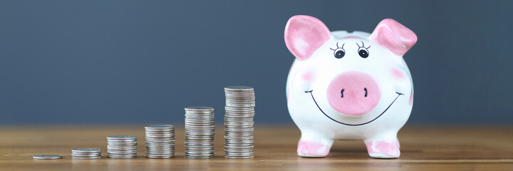 Pink piggy bank standing on table near heaps of coins