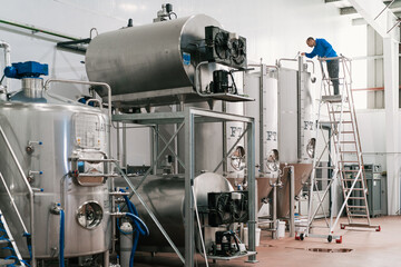 Brewer on ladder filling fermentation reservoir in beer factory