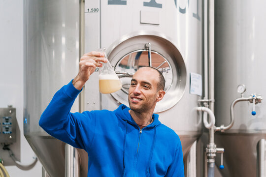 Smiling brewer with wort in flask in factory