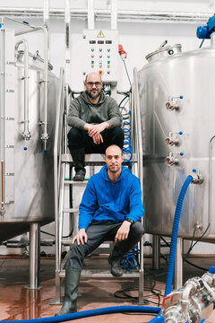 Smiling colleagues between professional equipment in beer factory