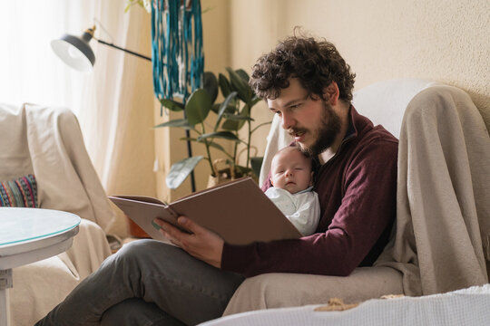 Father with newborn baby reading book at home