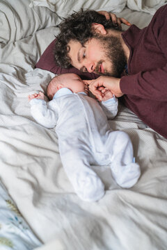 Father with newborn baby resting on crumpled bed at home