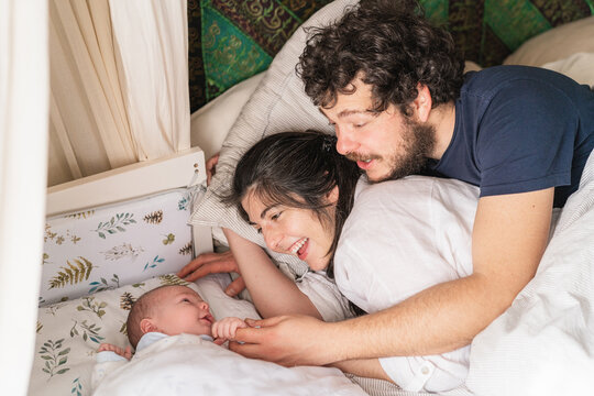 Smiling family with newborn baby resting in bed
