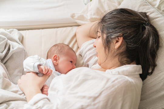 Mother breastfeeding newborn child on bed in house