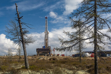 Natural landscape of the northern oil and gas field with a drilling rig for drilling deep wells. Spring coniferous forest, blue cloudy sky