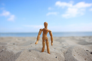 Close up of wooden mannequin standing in the sand on the beach in front of ocean in summer.
