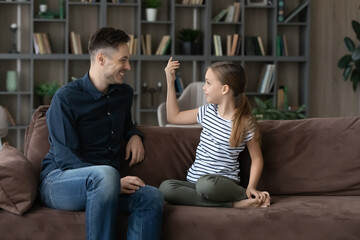 Obraz premium Smiling loving young Caucasian father relax on sofa in living room talk speak with teen daughter. Happy caring dad with girl child have fun rest on couch at home enjoy family weekend time together.