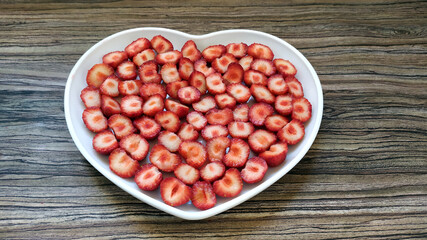The sliced strawberries are in a heart-shaped plate. A romantic serving of a healthy dessert.
