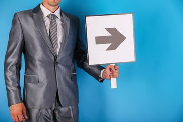 businessman holds a sign with an arrow on a blue background. a man wearing suit points to something by an arrow sign 