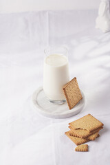 A glass of milk on a marble plate on a white table cloth and freshly baked cookies
