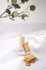 A glass of milk on a marble plate on a white table cloth and freshly baked cookies