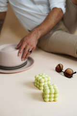 A pastel green bubble candle on an beige colored seamless background, sunglasses, a hat, and a male in the background