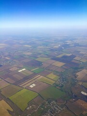 Top view of the earth with rectangular fields and blue sky in summer from the window of a flying air plane wing over the land. 