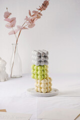 Several bubble candles, grey, patel green and beige stacked on top of each other on white table cloth