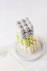 Several bubble candles, grey, patel green and beige stacked on top of each other on white table cloth