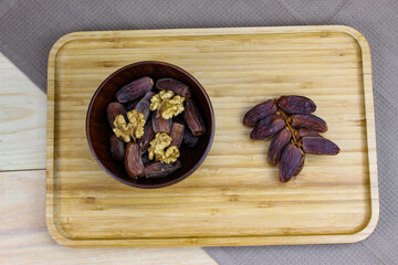 Twig with dates on a wooden tray. Wooden bowl with dates and walnut kernels. Fruit on a wooden tray. Fruit dates. Walnut kernels.