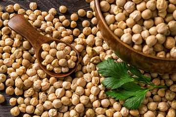 Raw chickpeas in a wooden spoon on a scattered chickpea beans near a wooden bowl with chick peas on a table. Vegetable protein and fibers source. Hummus and healthy vegetarian food ingredient.