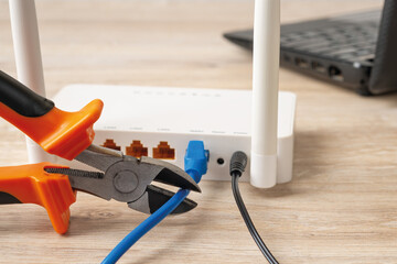 Close-up of wire cutters ready to cut the network cable connected to white wi-fi wireless router on...