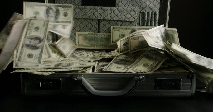 Close up shot of 100 US dollars bills being blown away by the wind from metal briefcase. Cash falling from the case - cash flow, finance concept 4k footage
