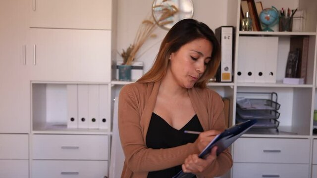 Young colombian woman manager holding clipboard in modern office. High quality FullHD footage