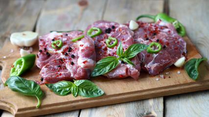 Raw pork steaks with spices on a wooden board.