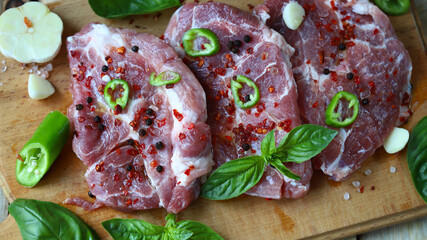 Raw pork steaks with spices on a wooden board.