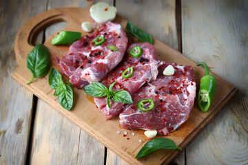 Raw pork steaks with spices on a wooden board.