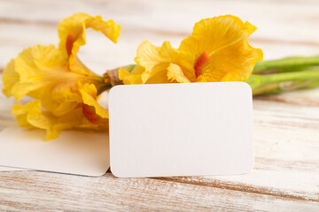 White business card with iris yellow flowers on white wooden background. side view, copy space.