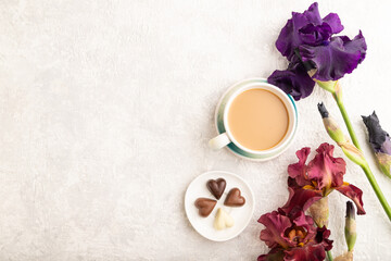 Obraz na płótnie Canvas Cup of cioffee with chocolate candies and purple and burgundy iris flowers on gray concrete background. top view, copy space.