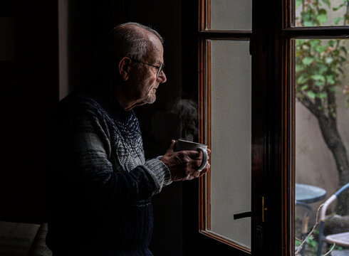 Older man with cup of tea looks melancholy out the window