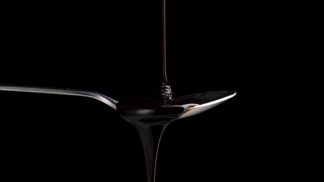 Liquid chocolate pouring into a spoon on black background.