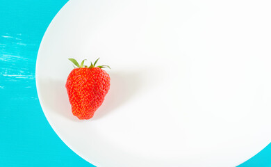 One ripe strawberry on a white plate